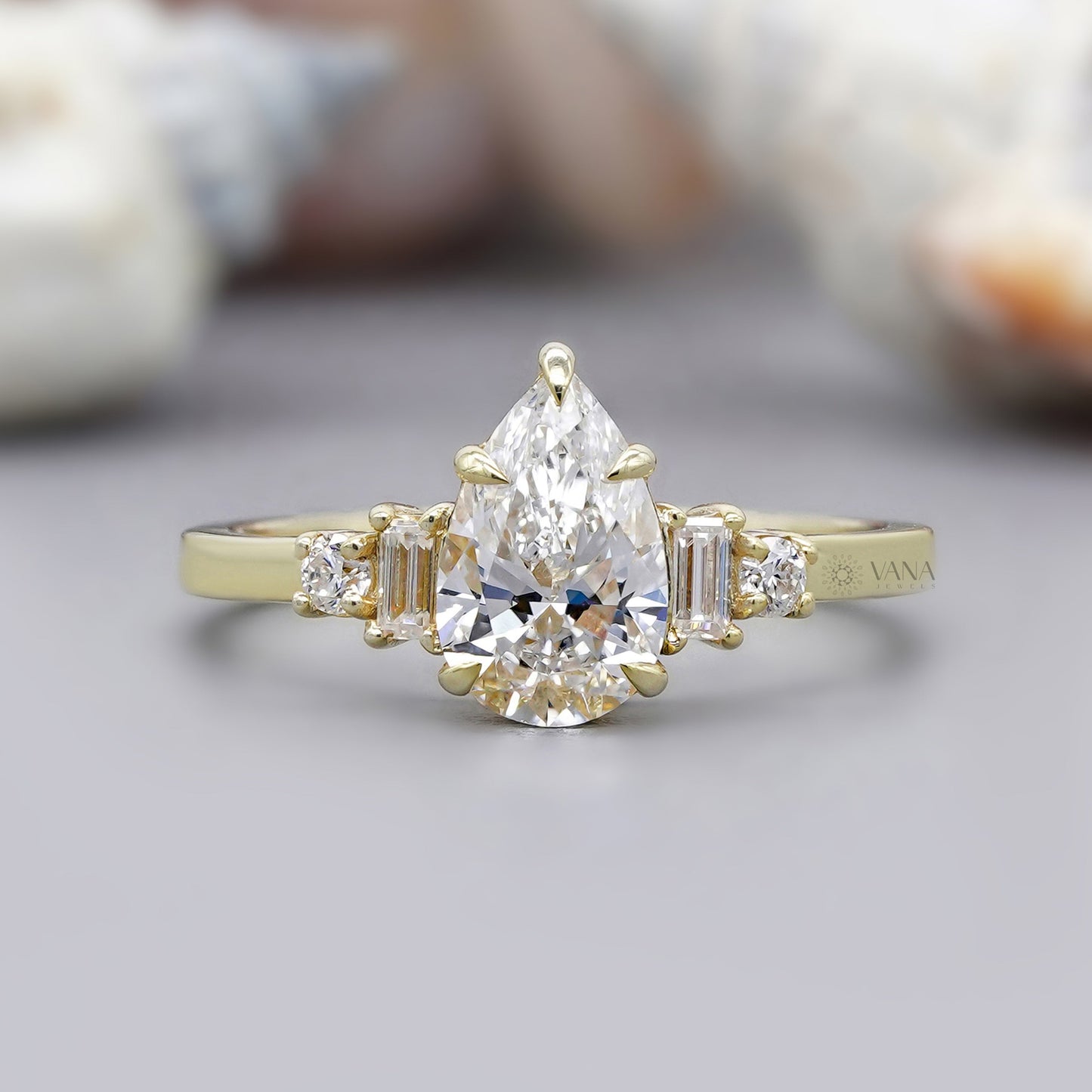 Gold ring with a pear-shaped diamond and baguette side stones on a neutral background