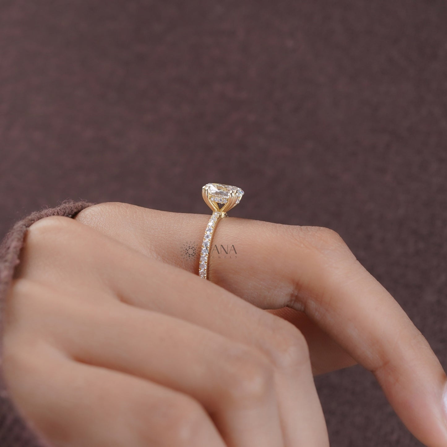 Hand wearing a gold ring with a diamond on a brown background