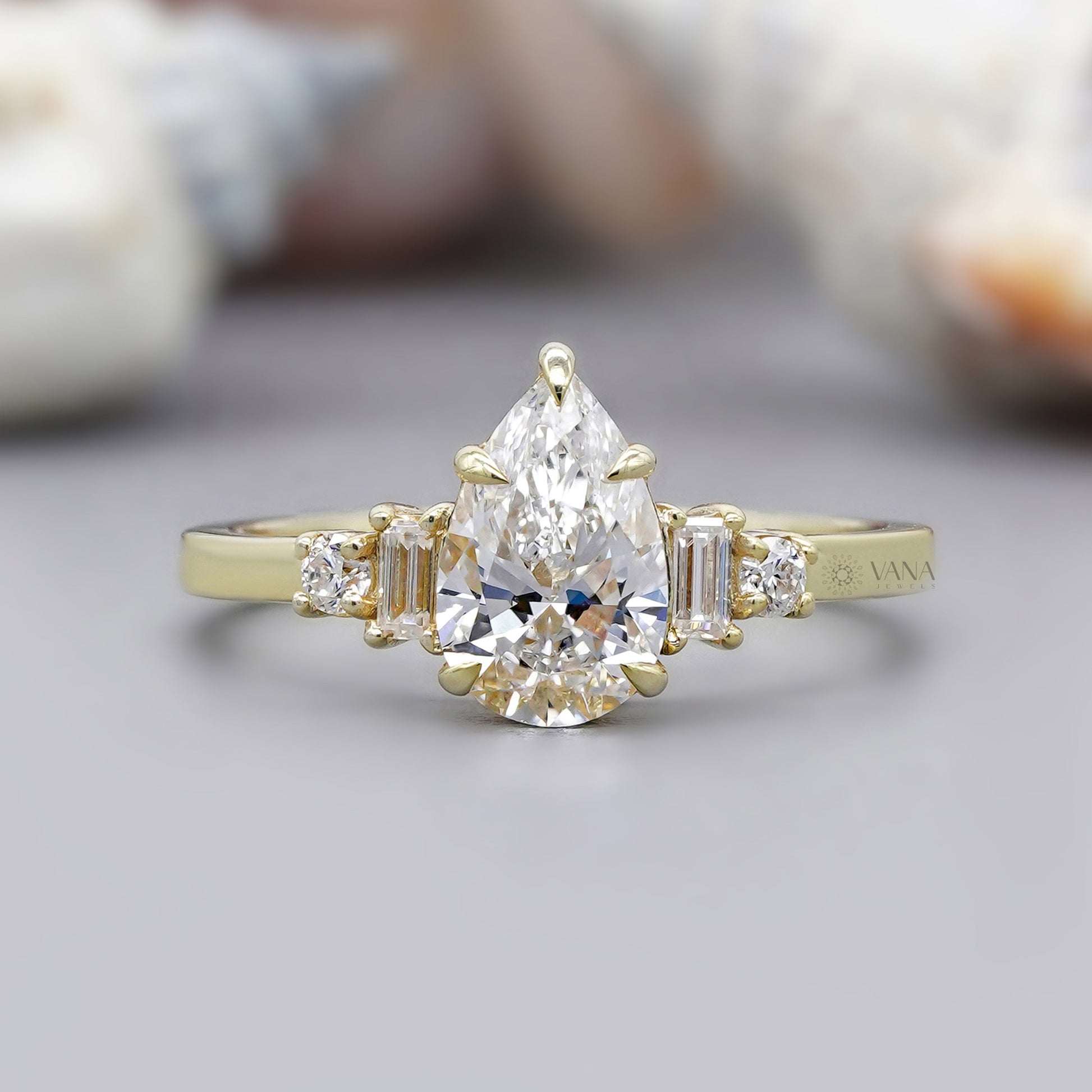 Gold ring with a pear-shaped diamond and baguette side stones on a neutral background