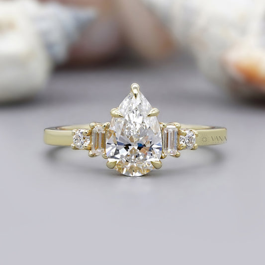 Gold ring with a pear-shaped diamond and baguette side stones on a neutral background