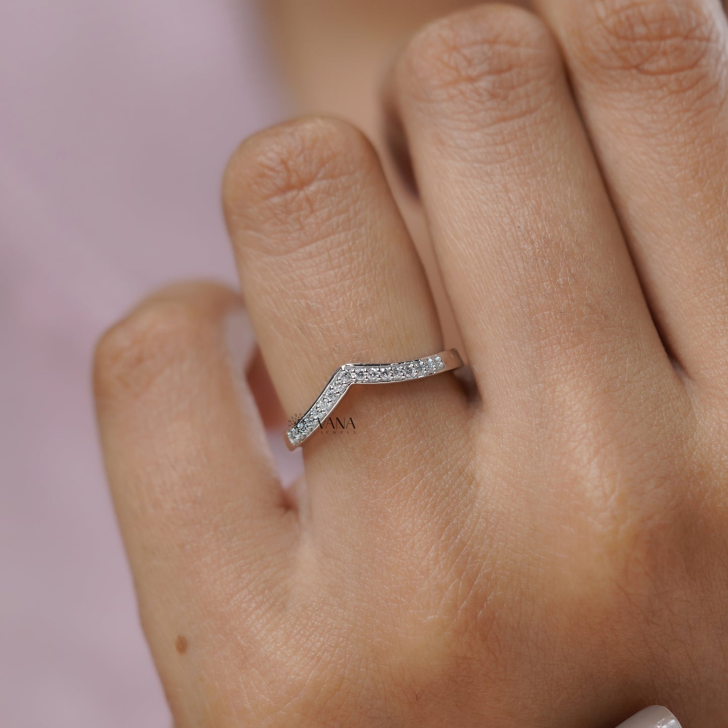 Silver ring with small diamonds on a finger against a pink background