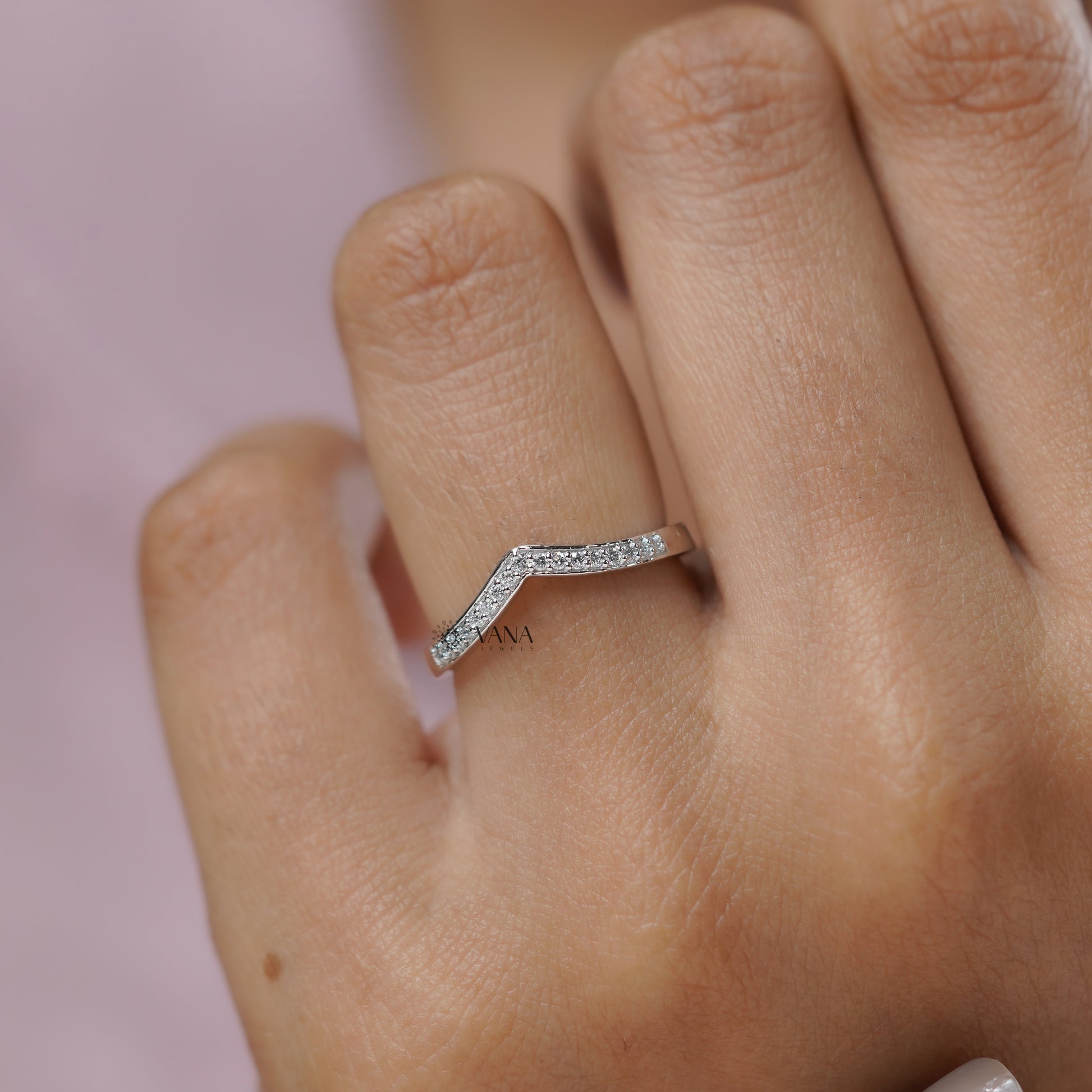 Silver ring with small diamonds on a finger against a pink background